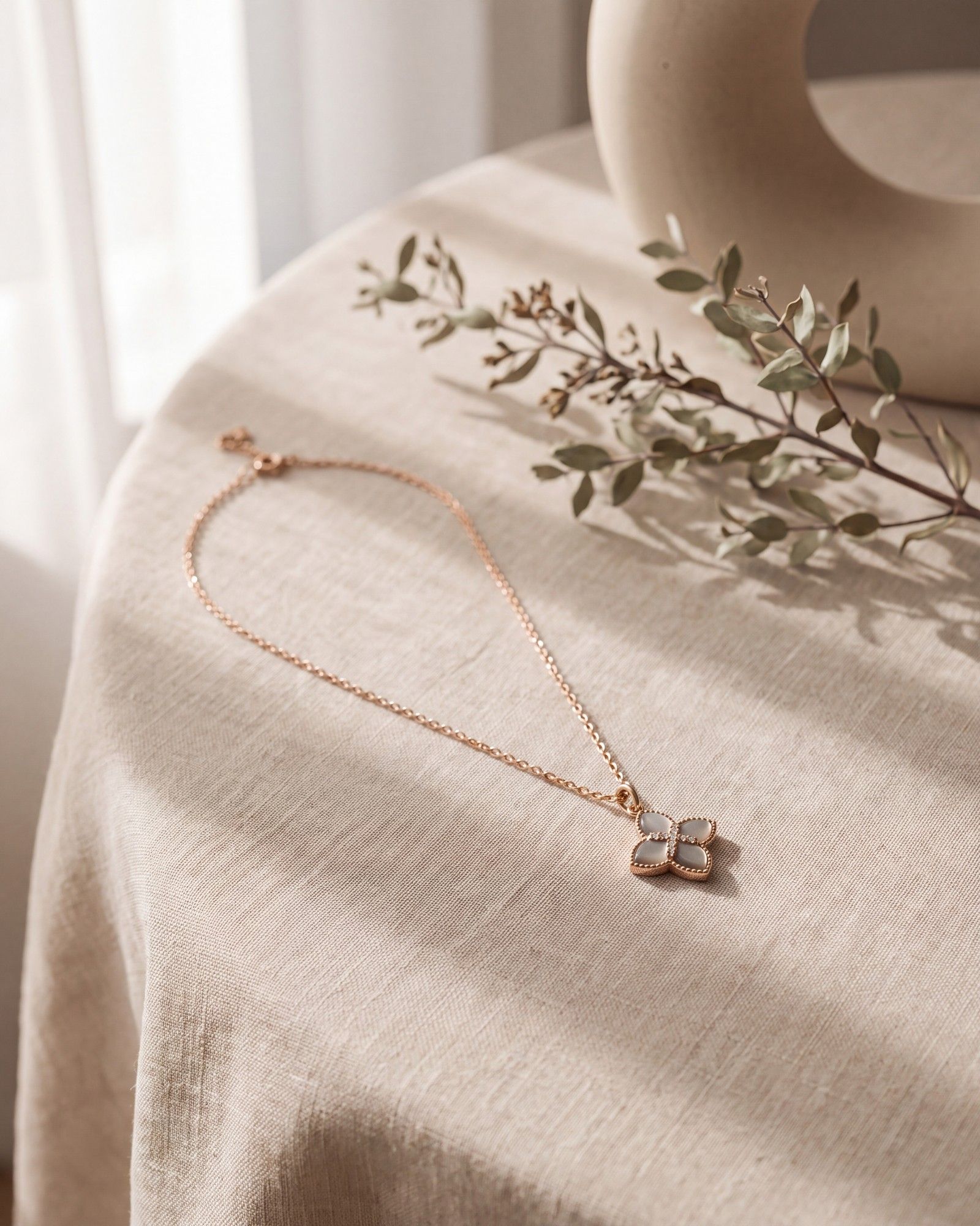 The same necklace on light linen next to a twig in soft window light; mother-of-pearl pendant unchanged