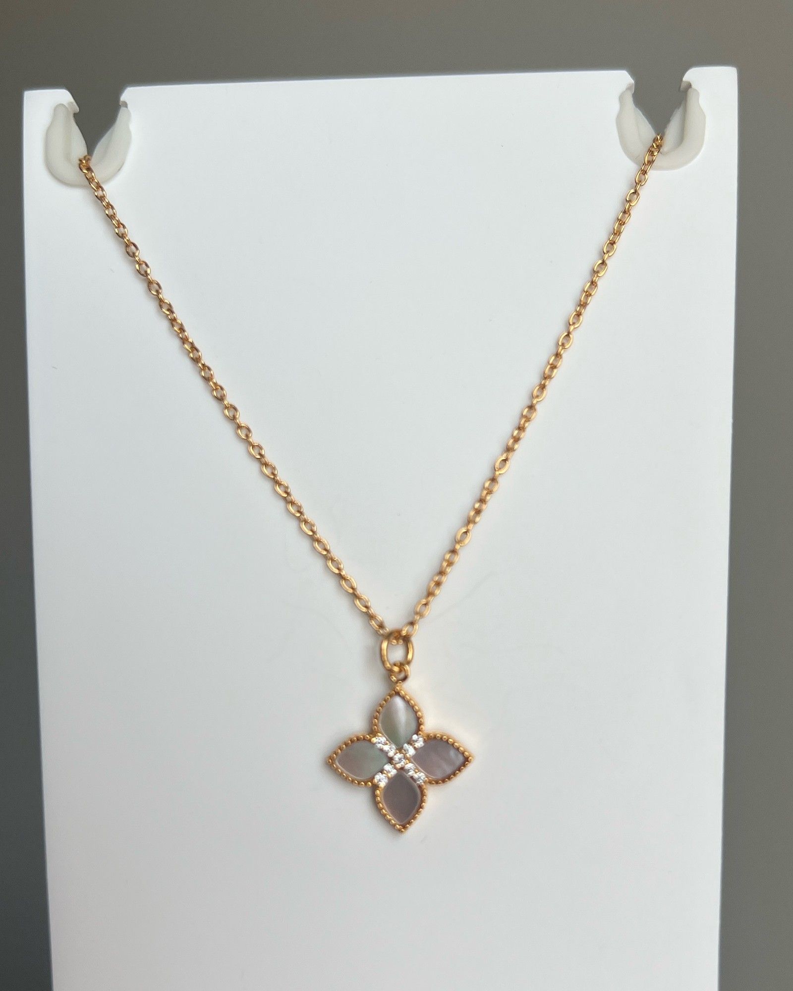 Phone photo of a rose gold necklace with a four-petal mother-of-pearl pendant on a white display card