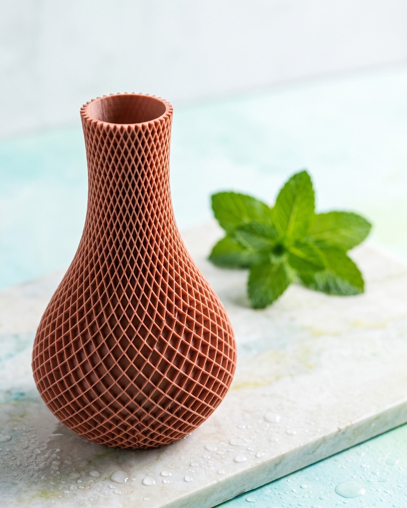 Dieselbe Vase auf einer hellen Steinplatte mit Wassertropfen und frischer Minze in kühlem Tageslicht; Form, Rautenmuster und Farbe unverändert